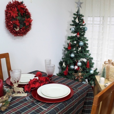 Mesa de jantar decorada para Natal com pratos, copos, arranjo de flores e rena, árvore de Natal e guirlanda vermelha na parede