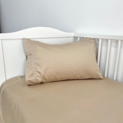 Cama branca de criança com roupa de cama bege e detalhes de renda