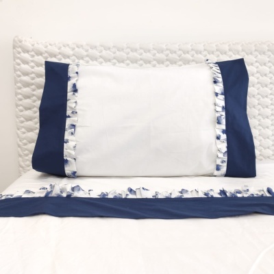 Almofada branca com laterais azul-marinho e fita estampada azul em cama com cabeceira acolchoada branca