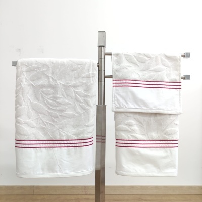 Conjunto de toalhas brancas com padrão de folhas e listra vermelha penduradas em suporte metálico