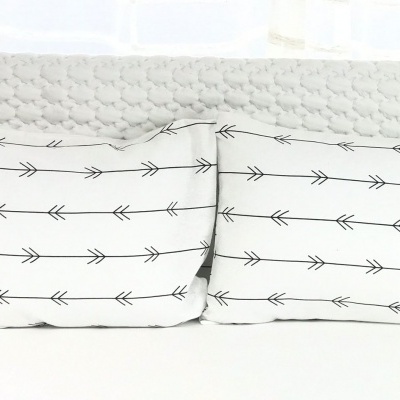 Duas almofadas com padrão de setas pretas em fundo branco numa cama branca com cabeceira acolchoada.