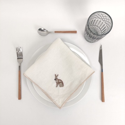 Mesa posta com talheres de cabo em madeira, dois pratos brancos, guardanapo com bordado de coelho e copo de vidro decorativo