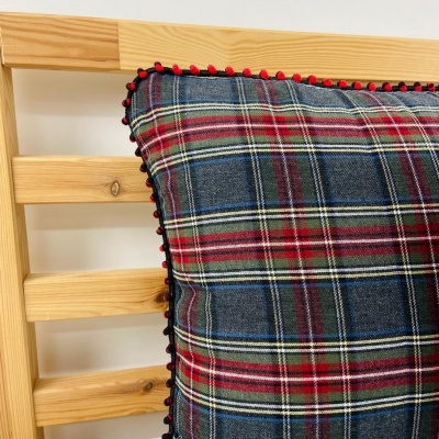 Almofada xadrez azul e vermelha com borda de pompons sobre estrutura de madeira clara