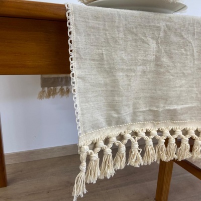 Toalha de mesa bege claro com franjas de macramé pendurada numa mesa de madeira.