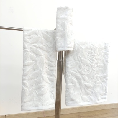 Toalhas brancas com padrão de folhas penduradas num suporte metálico num ambiente interior