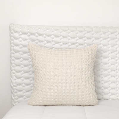 Almofada bege claro com padrão texturizado sobre cabeceira branca com padrão de corações em relevo