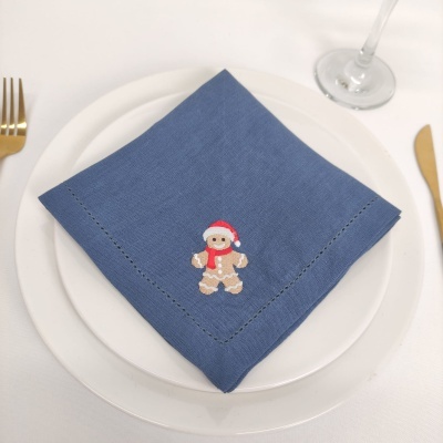 Guardanapo azul com bordado de boneco de gengibre num prato branco com talheres dourados