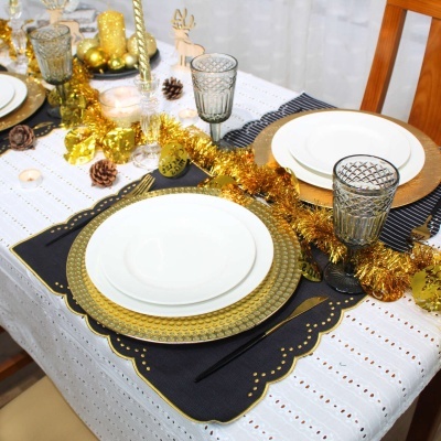 Mesa de jantar decorada com pratos brancos, bases douradas, copos cinza texturizados e decoração festiva dourada