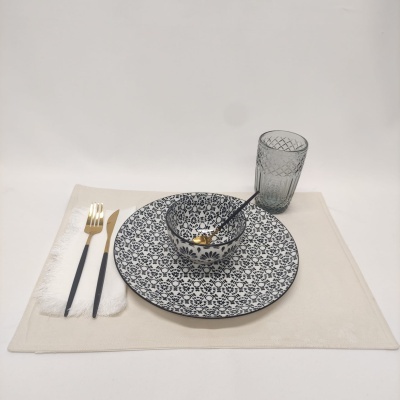 Conjunto de louça com prato e tigela azul e branca, copo cinza e talheres dourados com cabo preto