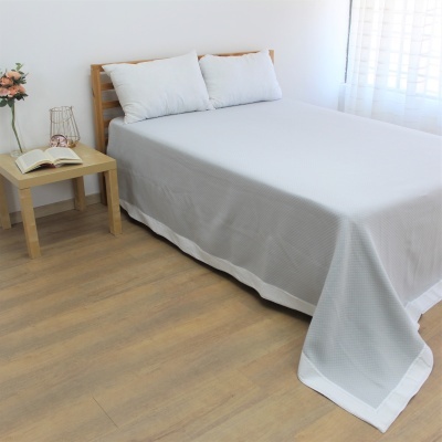 Quarto com cama de madeira clara e colcha branca com mesa de cabeceira e flores