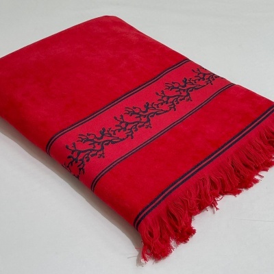 Toalha de banho vermelha com bordado azul escuro e franjas numa superfície branca.