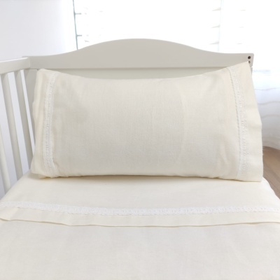 Travesseiro e lençol cremosa com rendas numa cama branca