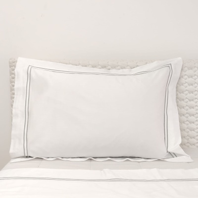 Almofada branca com bordado cinzento sobre cama branca e cabeceira estampada