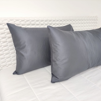 Almofadas cinzentas em tecido liso sobre colchão branco com cabeceira texturizada