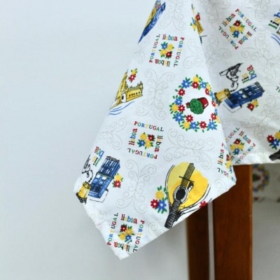 Toalha de mesa branca estampada com motivos portugueses coloridos cobrindo mesa de madeira