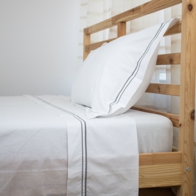 Cama de madeira clara com roupa de cama branca com riscas cinzentas