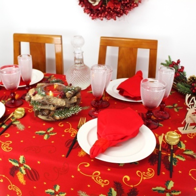 Mesa de jantar decorada para Natal com toalha vermelha, pratos brancos, guardanapos vermelhos, copos com base vermelha, talheres dourados e centro de mesa com vela
