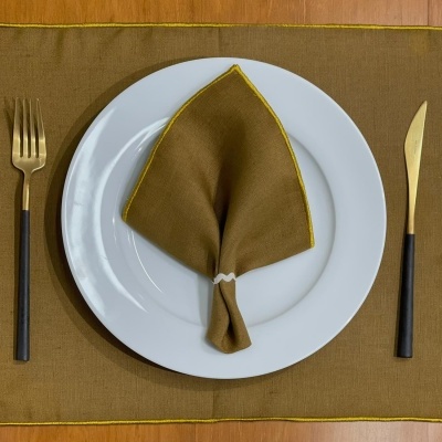 Jogo americano castanho com costura amarela, guardanapo castanho com borda amarela em prato branco com talheres preto e dourado