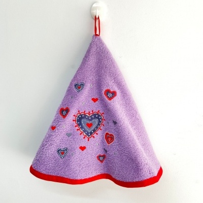 Pano triangular lilás com bordas vermelhas e corações bordados, pendurado numa parede branca