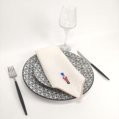 Mesa posta com pratos cerâmicos brancos e pretos, guardanapo branco bordado, talheres pretos e copo de vidro