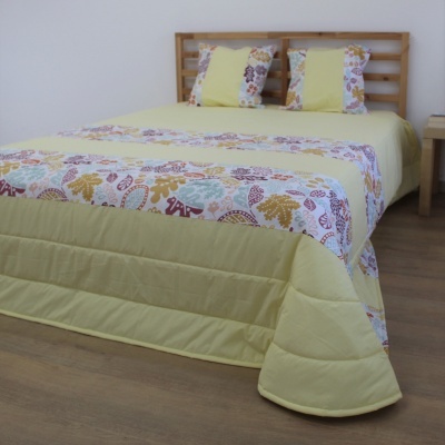Colcha e almofadas amarelas com padrão floral em cama com cabeceira de madeira