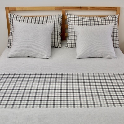 Cama com conjunto de lençóis e almofadas em padrão xadrez cinza e liso com cabeceira de madeira