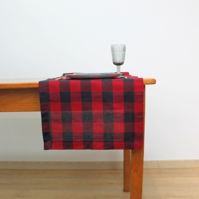Toalha de mesa xadrez vermelho e preto sobre mesa de madeira com prato e copo.