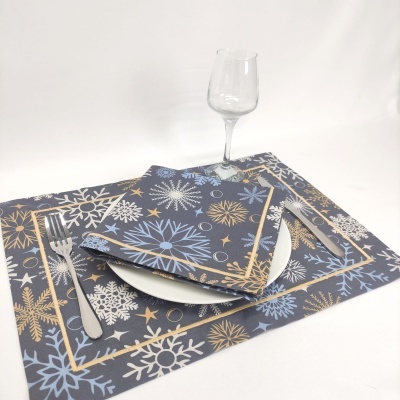 Guardanapos e bases de prato com padrão de flocos de neve em azul, branco e dourado, com talheres e copo de vidro