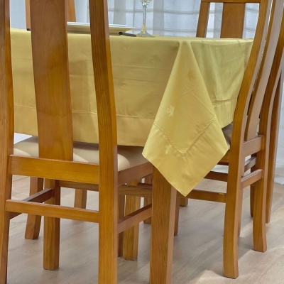 Mesa de jantar em madeira clara com toalha amarela e quatro cadeiras de madeira