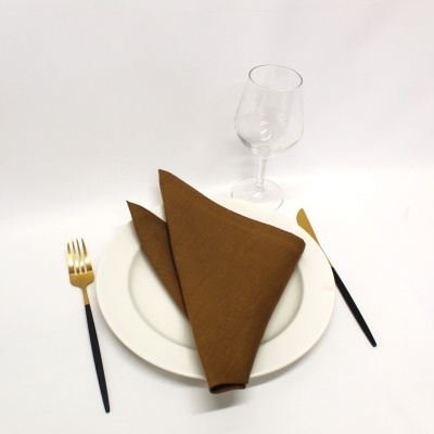 Conjunto de prato branco, guardanapo castanho, talheres com cabos pretos e extremidades douradas, copo de vidro transparente