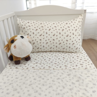 Cama de bebé com lençóis bege claro estampados e peluche vaca