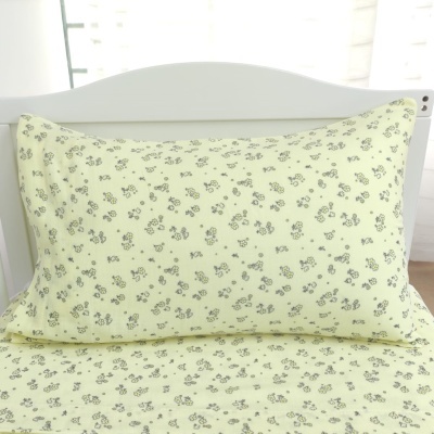 Travesseiro amarelo claro com padrão de flores cinza escuro numa cama com cabeceira branca