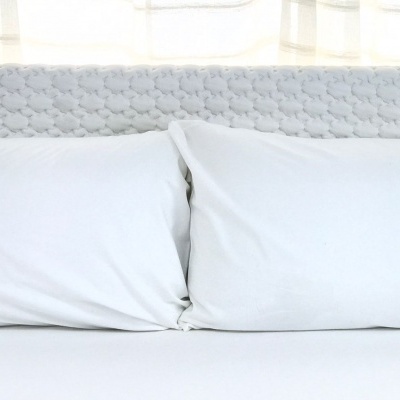 Cabeceira de cama cinzenta com almofadas e lençol brancos