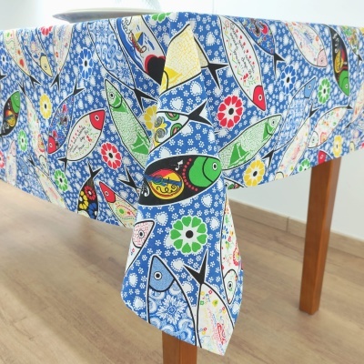 Toalha de mesa azul com peixes coloridos e flores, posta numa mesa de madeira