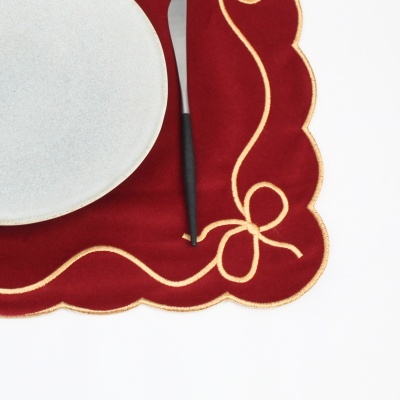 Guardanapo vermelho com bordas onduladas e decoração dourada, prato branco e talher