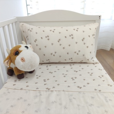 Conjunto de roupa de cama infantil bege com estrelas castanhas num berço branco e peluche de vaca