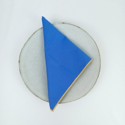 Guardanapo azul dobrado com borda amarela em prato branco com borda castanha