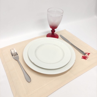 Conjunto de jantar branco com talheres de metal e copo vermelho sobre pega-beber bege