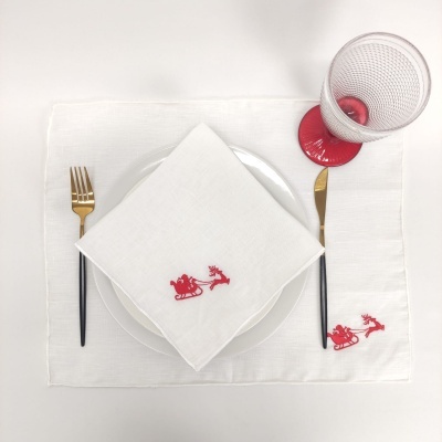 Mesa posta com jogo americano, guardanapo com bordado vermelho, talheres, prato branco e copo com pé vermelho