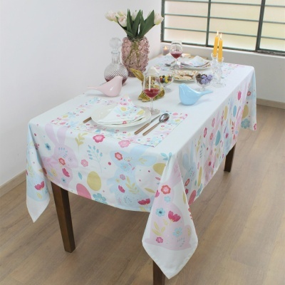 Toalha de mesa branca com padrão floral colorido em mesa de madeira posta com louça, copos, velas e flores