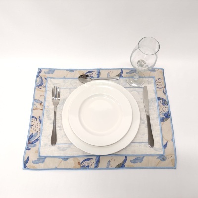 Conjunto de jantar com pratos brancos, talheres de metal e taça de vidro sobre individual azul e bege