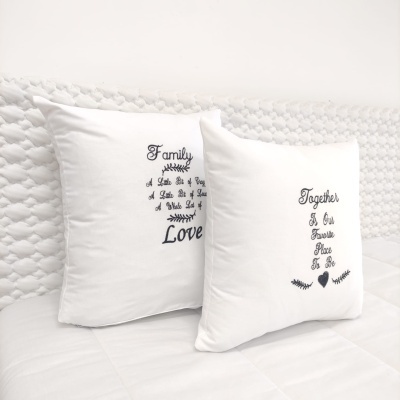 Duas almofadas brancas com texto preto numa cama branca com cabeceira de rattan