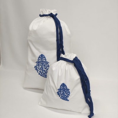 Duas bolsas de tecido branco com padrão azul e cordões azuis sobre fundo cinza claro.