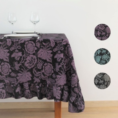 Toalha de mesa jacquard com padrão floral em roxo, azul e cinza sobre uma mesa de madeira com duas taças e pratos.