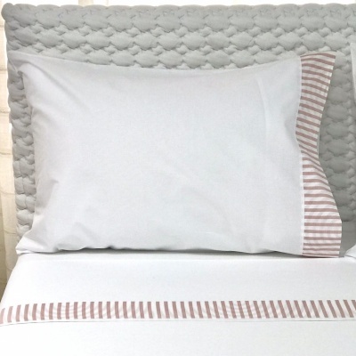 Travesseiro branco com fronha listrada em cama com lençol branco e cabeceira azul texturizada