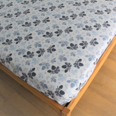 Lençol ajustável branco com padrão de folhas azuis e pretas em cama de madeira clara