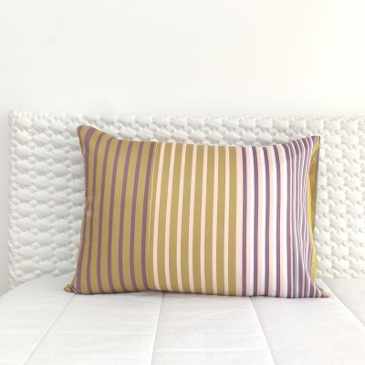 Almofada com riscas verticais em tons amarelo, bege, branco e roxo sobre colchão branco