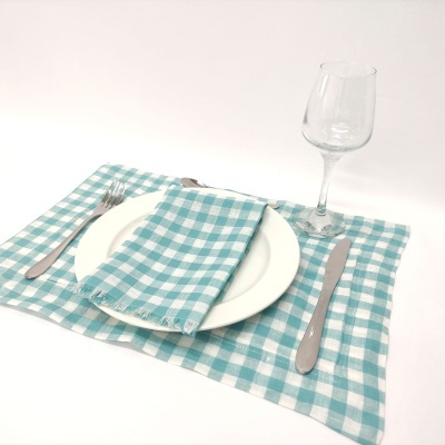 Conjunto de mesa com prato branco, talheres, guardanapo e copo sobre individual xadrez azul e branco