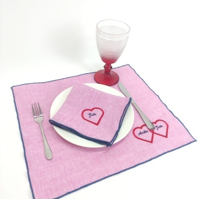 Conjunto de mesa com individual e guardanapo rosa bordados com corações e nomes, prato branco, talheres e copo vermelho
