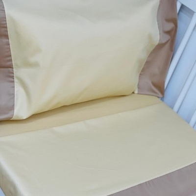 Roupas de cama bege com bainhas castanhas numa estrutura branca